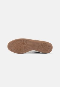 Vit sneaker med böjd design, texturerad sula i gummimaterial och cirkulärt mönster i sulan. Har subtil märkning på sidan.