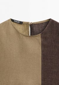 Närbild på en tvåtonad brun texturerad blus med rund halsringning, knappstängning baktill och en synlig Massimo Dutti-label.