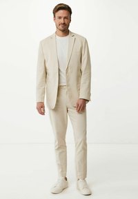 Beige linnekostym med skräddarsydd kavaj och figurnära byxor. Matchad med en enkel vit t-shirt och vita sneakers. Slät textur, modern design.