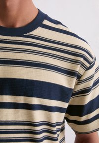 Short-sleeve, crew-neck shirt in beige with navy horizontal stripes, textured fabric, and contrasting ribbed neckline.