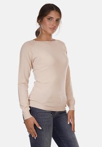 Maglione lungo beige chiaro a maniche lunghe realizzato in morbido materiale a maglia. Presenta un collo rotondo e una vestibilità aderente, abbinato a jeans blu scuro.