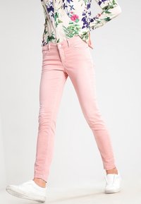 Světle růžové skinny džíny vyrobené z bavlněné směsi s pěti kapsami a pasem s poutky na opasek, v kombinaci s kostkovanou květinovou košilí.