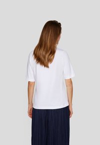 Weißes Baumwoll-T-Shirt mit kurzen Ärmeln, entspannter Schnitt und Rundhalsausschnitt, getragen über einem plissierten marineblauen Rock.