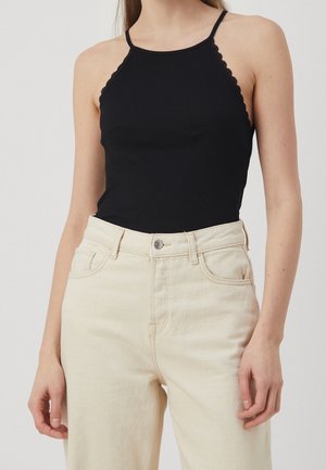 Schwarzes, geripptes Tanktop mit wellenförmigen Trägern, kombiniert mit hoch taillierten, cremefarbenen Denim-Jeans mit Knopfleiste und seitlichen Taschen.