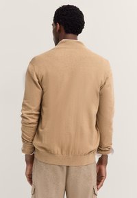 Maglione a maglia color sabbia con colletto, polsini e vita a costine. Texture liscia, design aderente, che mostra una vista posteriore semplice e pulita.