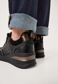 Sneaker neri con una finitura testurizzata, dettagli in bronzo e un design elegante. Il tallone presenta una striscia di bronzo a contrasto per un tocco di dettaglio in più.