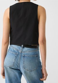 Black cropped tank top with a round neckline, paired with light blue high-waisted denim jeans featuring large back pockets and a subtle fade.