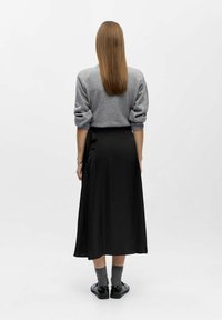 Grå sweater med opkrøllede ærmer, sammen med en sort, mellemlang nederdel. Sorte sko og grå sokker fuldender outfittet.