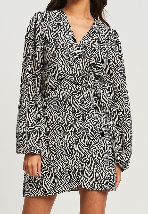 Robe à rayures zébrées noir et blanc avec un design portefeuille, manches longues bouffantes et un détail noué à la taille. Texture du tissu lisse.