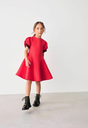 Rotes Kleid mit Puffärmeln, strukturiertem Stoff mit geprägten Mustern. Getragen mit schwarzen Schnürkampfstiefeln. Einfaches A-Linien-Design.