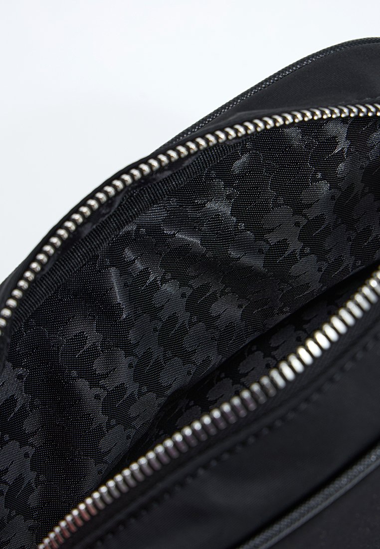 Mochila de nylon negra con una apertura con cremallera, que presenta un interior texturizado negro con un patrón sutil y detalles en cremallera plateados.