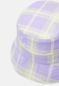 Bucket-Hut in Lavendel mit einem karierten Muster aus gelben und grauen Linien. Weiches Textilmaterial mit gesticktem Logodetail.