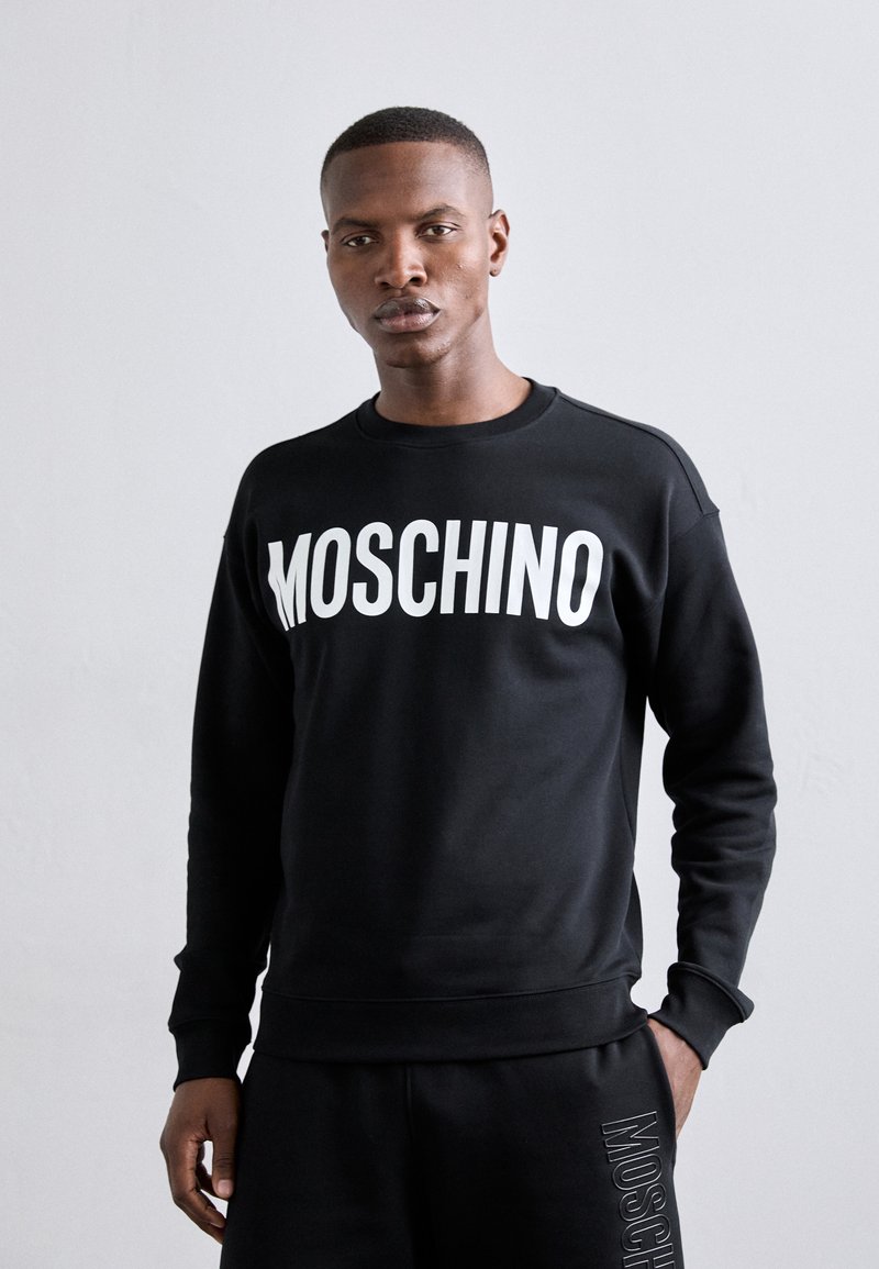 Sudadera negra con un audaz logo blanco "MOSCHINO" en el frente, con cuello redondo y puños y dobladillo acanalados. Fabricada en suave tejido de algodón.