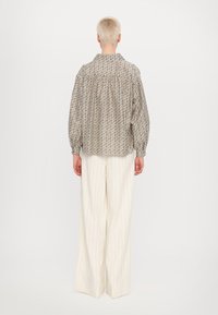 Mønstret bluse med løs pasform, i dempede beige- og bruntoner. Kombinert med høyhælte bukser i kremfarvet med striper.