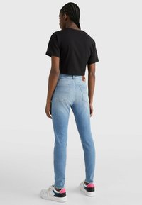 Vaqueros ajustados de un azul claro, confeccionados en denim, combinados con una camiseta negra corta y zapatillas blancas con acentos coloridos. Bolsillos traseros visibles.