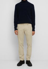 Marinblå turtlenecktröja, beige chinos och svarta ankelstövlar. Tröjan har en mjuk textur, medan byxorna har en rak passform.