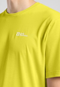 T-shirt in cotone giallo brillante con collo rotondo e maniche corte, caratterizzato da un piccolo logo bianco sul lato sinistro del petto. Texture liscia, vestibilità casual.