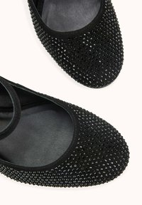 Chaussures en cuir verni noir à bout arrondi, ornées de petits strass noirs, avec une surface lisse légèrement texturée.