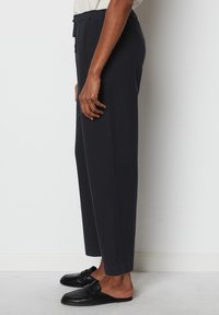 Black, tapered sweatpants made of soft fabric with an elastic waistband, side pockets, and cuffed ankles, paired with black slide-on shoes.