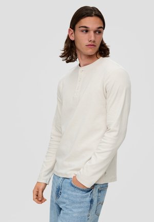 Langermige, off-white henley shirt met drie knopen, zachte textuur en losse pasvorm, gecombineerd met lichtblauwe denim jeans.