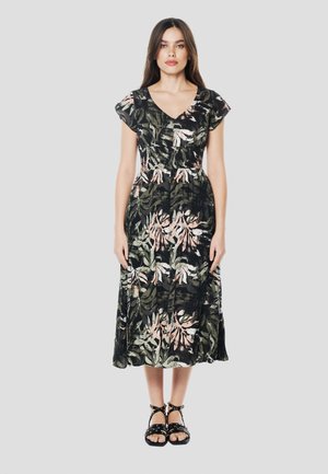 Vestido largo floral en negro con patrones de hojas verdes y rosas. Escote en V y mangas con vuelo, hecho de tela ligera. Sandalias negras completan el look.