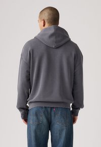 Γκρι φούτερ με κουκούλα και άνετη γραμμή, με ριμπ τελείωμα και μανσέτες. Το ύφασμα φαίνεται μαλακό με λεία υφή.