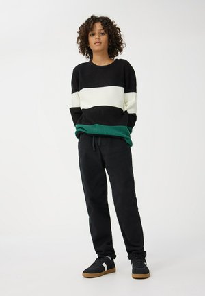 Sweter w czarno-białe paski z zielonym wykończeniem, połączony z czarnymi spodniami i czarnymi trampkami z białym paskiem. Strukturana dzianina.