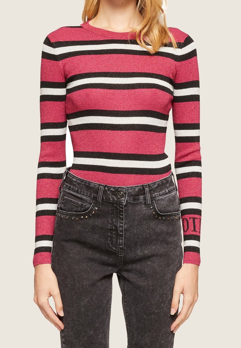 Femme portant un t-shirt ajusté à manches longues avec des rayures horizontales rose, noir et blanc, associé à un jean noir taille haute avec des détails cloutés.
