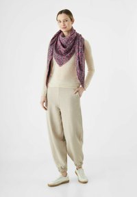 Une écharpe en imprimé léopard rose et gris drapée sur un pull beige clair et un jogging, assortie à des baskets blanches avec une semelle beige.