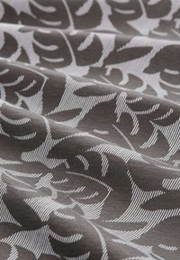 Tkanina o ciemnoszarym tle z białym wzorem liści. Tekstura jest gładka, z wyraźnymi liniami tworzącymi kształty liści.