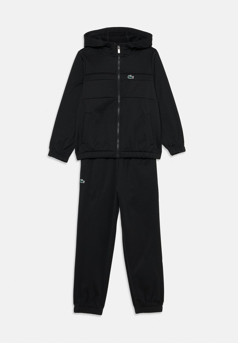 Survêtement noir comprenant un hoodie zippé avec une poche kangourou et un pantalon assorti. Les deux sont dotés de poignets élastiques et d'un petit accent logo vert.