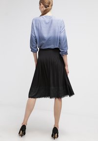 Blusa azul con estampado y mangas de tres cuartos, combinada con una falda negra con pliegues que presenta un ribete de encaje en el dobladillo y zapatos de tacón clásicos.