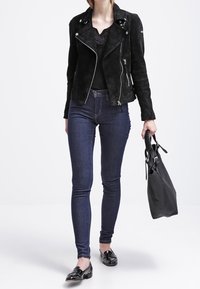 Giacca biker in suede nera con zip argentate, top nero, jeans skinny blu scuro e mocassini neri verniciati. Porta una borsa nera.