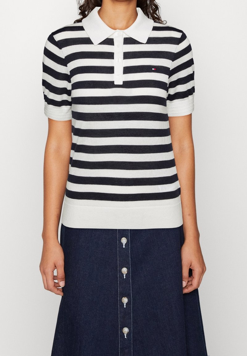 Femme portant un polo à rayures horizontales noires et blanches à manches courtes et une jupe en denim foncé avec des boutons à l'avant.