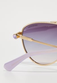 Súťažné okuliare majú zlatý kovový rám s gradientnými fialovými sklíčkami. Rámy majú levanduľový akcent a brandingu Swarovski.