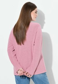 Różowy sweter o teksturze, w luźnym kroju z długimi rękawami i zaokrąglonym dołem, w połączeniu z jasnoniebieskimi dżinsami.