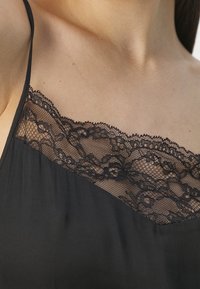 Camisole noire avec des bretelles fines, ornée de jolis détails en dentelle noire le long de l'encolure. Texture lisse avec un design ample et fluide.