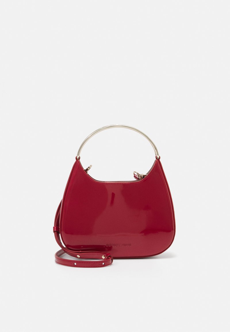 Red patent leather handbag with a unique curved design, featuring a metallic handle and detachable strap. Glossy, smooth texture.