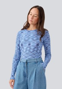 Hosszú ujjú, kék felső, texturált mintával, kerek nyakkivágással és slim fit szabással, világoskék, magas derekú nadrággal párosítva.