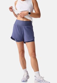 Leichte, lila Sportshorts mit einem breiten Bund, gestuftem Design und integrierter Unterhose. Kombiniert mit einem weißen Tanktop und Turnschuhen.