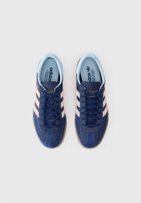 Tumedad suėdidest sneakerid roosa triibuga, sinise sisestruktuuriga ja pruunist kummist tallaga. Omab paelu ja kuldset brändikirja.