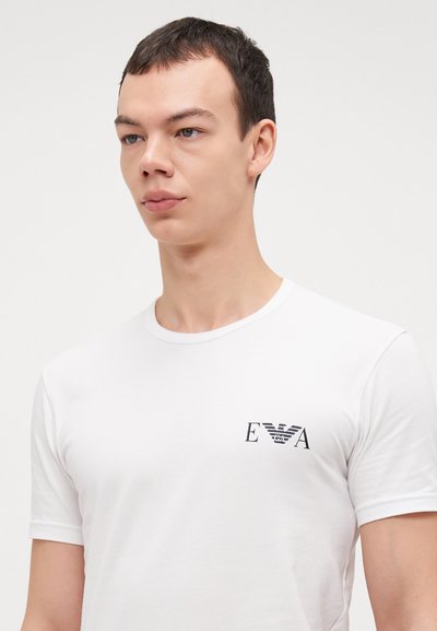 T-shirt en coton blanc avec un col rond et des manches courtes, arborant un petit logo noir sur la zone gauche de la poitrine.