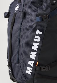 Marine ryggsekk med geometrisk mønster, som har hvit "MAMMUT" logo, holdbart stoff, justerbare stropper og svarte detaljer.
