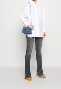 White cotton shirt with long sleeves, gray flared jeans with frayed hem, and a blue leather handbag with a chain strap and metal clasp. Orange sandals.