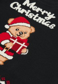 Schwarzer Strickpullover mit einem Bären im roten Weihnachtsmannanzug, der ein Geschenk hält, und dem Text "Frohe Weihnachten" in Weiß über dem Design.