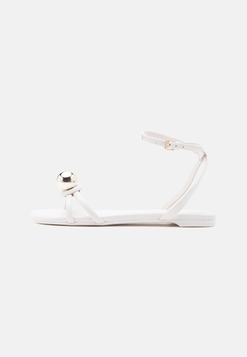 Balta plakana sandale ar plānām siksniņām, potītes sprādzi un lielu spīdīgu sudraba bumbu priekšējā pirksta daļā.