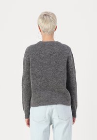 Grå uldtrøje med rund halsudskæring, ribbede manchetter og en afslappet pasform. Båret over lyseblå jeans, har den en struktureret overflade.