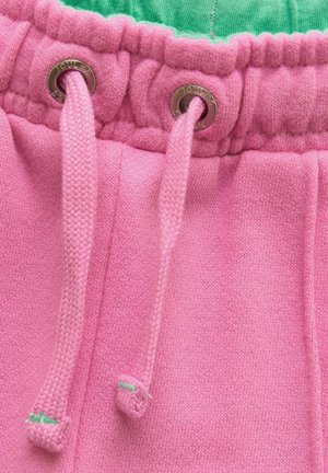 Nahaufnahme eines rosa Kordelzugs am Hüftbund weicher Stoffhosen mit Metallösen und einem grünen Innenbund.