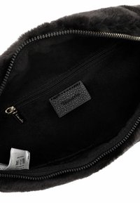 Interno della borsa nera foderato in pelliccia con una tasca con zip e etichetta in pelle testurizzata. La chiusura presenta una cerniera in tono oro con una fodera in tessuto.