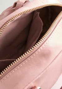 Wnętrze jasnoróżowej torby z tkaniny z złotym zamkiem błyskawicznym, charakteryzujące się gładką teksturą i wykończonymi szwami. Otwarty design ujawnia przestrzeń wewnętrzną.